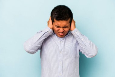 Mavi arka planda izole edilmiş genç İspanyol adam kulaklarını elleriyle kapatıyor..