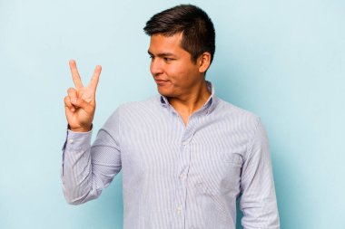 Mavi arka planda izole edilmiş genç İspanyol adam neşeli ve kaygısız parmakları olan bir barış sembolü gösteriyor..