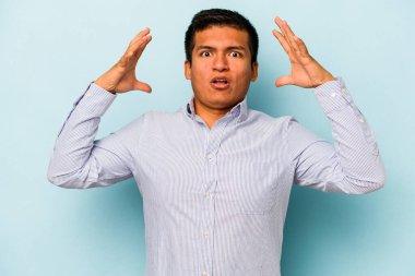 Latin kökenli genç bir adam mavi arka planda zaferi ya da başarıyı kutlarken şaşırmış ve şok olmuştu..