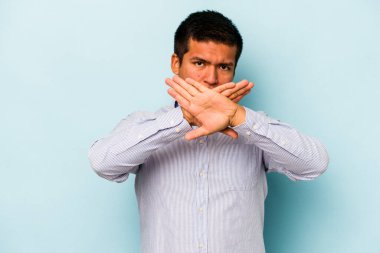 Genç İspanyol bir adam mavi arka planda izole edilmiş, inkar jesti yapıyor.