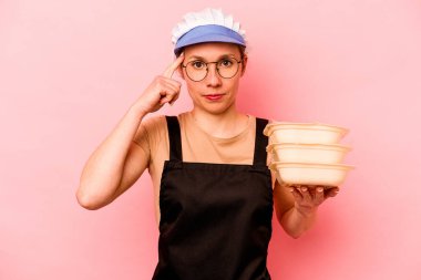 Genç aşçı, pembe arka planda izole edilmiş, parmağıyla tapınağı işaret eden, düşünen, bir göreve odaklanmış bir gönüllü kadın..