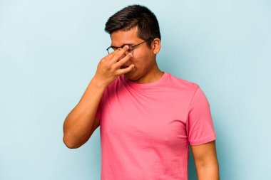 Genç İspanyol bir adam mavi arka planda izole edilmiş, başı ağrıyor, yüzüne dokunuyor..