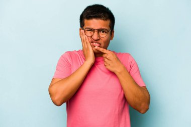 Genç İspanyol bir adam mavi arka planda izole edilmiş güçlü bir diş ağrısı, azıdişi ağrısı var..