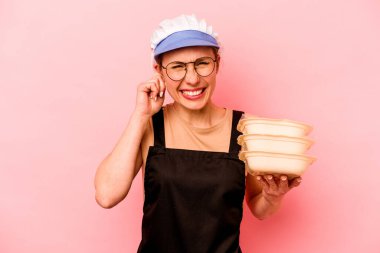 Genç aşçı gönüllü kadın pembe arka planda izole edilmiş kulakları elleriyle kapatıyor..