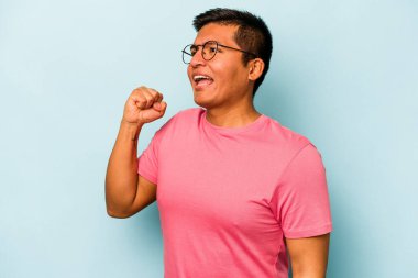 Mavi arka planda izole edilmiş genç İspanyol bir adam zaferi, tutkuyu ve coşkuyu kutluyor, mutlu bir ifade..