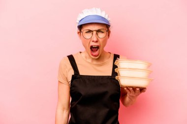 Genç aşçı gönüllü kadın pembe arka planda izole edilmiş çok kızgın ve agresif çığlıklar atıyor..