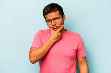 Latin kökenli genç bir adam mavi arka planda izole edilmiş. Bir strateji planlıyor, bir iş yolu düşünüyor..