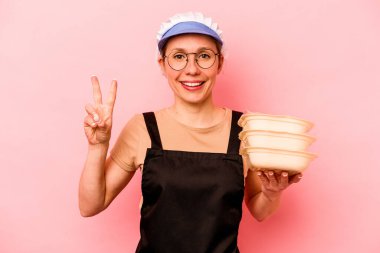 Genç aşçı gönüllü kadın pembe arka planda izole edilmiş iki numarayı parmaklarıyla gösteriyor..