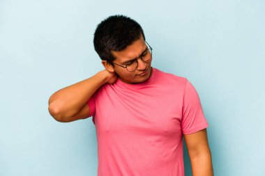 Genç İspanyol bir adam mavi arka planda izole edilmiş. Stres yüzünden boynu ağrıyor. Masaj yapıyor ve elle dokunuyor..