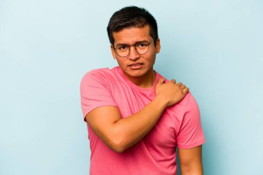 Mavi arka planda izole edilmiş genç İspanyol bir adam omuz ağrısı çekiyor..