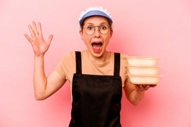 Pembe arka planda izole edilmiş genç aşçı kadın hoş bir sürpriz alıyor, heyecanlı ve el kaldırıyor..