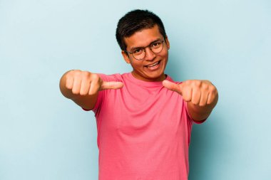 Genç İspanyol adam mavi arka planda izole edilmiş. Baş parmağını kaldırıyor, gülümsüyor ve kendinden emin..