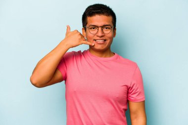 Mavi arka planda izole edilmiş genç bir İspanyol, parmakları olan bir cep telefonu hareketi gösteriyor..