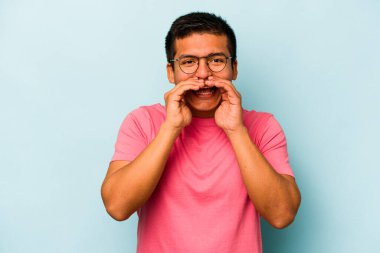 Genç İspanyol bir adam mavi arka planda izole edilmiş. Dedikodu yapıyor, bir şeyleri bildiriyor..