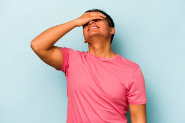 Mavi arka planda izole edilmiş genç İspanyol adam ellerini başının üstünde tutarak neşeyle gülüyor. Mutluluk kavramı.