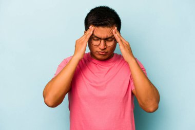 Genç İspanyol adam mavi arka planda izole edilmiş tapınaklara dokunuyor ve baş ağrısı çekiyor..