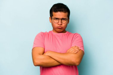 Mavi arka planda izole edilmiş genç bir İspanyol omuz silker ve gözleri açık kalır..