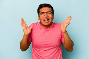 Genç İspanyol bir adam mavi arka planda izole edilmiş. Hoş bir sürpriz bekliyor. Heyecanlı ve el kaldırıyor..