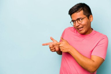 Genç İspanyol adam mavi arka planda izole edilmiş başparmak uzakta, gülüyor ve kaygısız.