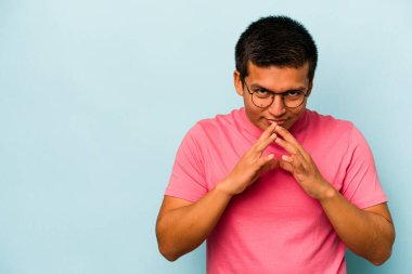 Latin kökenli genç bir adam mavi arka planda izole edildi. Aklında bir plan kuruyor, bir fikir kuruyor..