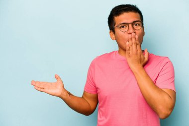 Mavi arka planda izole edilmiş genç İspanyol adam, avuç içinde kopya alanı tutmaktan etkilenmiş..