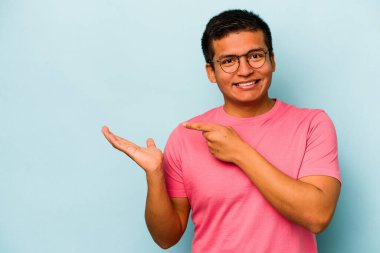 Mavi arka planda izole edilmiş genç İspanyol bir adam heyecanlı bir şekilde avuç içinde bir kopyasını tutuyor..