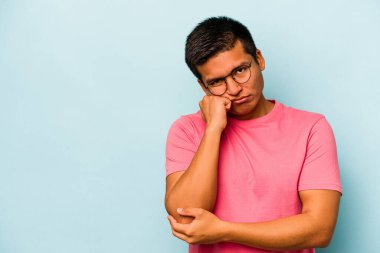 Mavi arka planda izole edilmiş, üzgün ve dalgın hisseden genç bir İspanyol fotokopi odasına bakıyor..