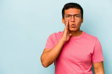 Mavi arka planda izole edilmiş genç İspanyol bir adam gizli bir sıcak fren haberi veriyor ve yana bakıyor.