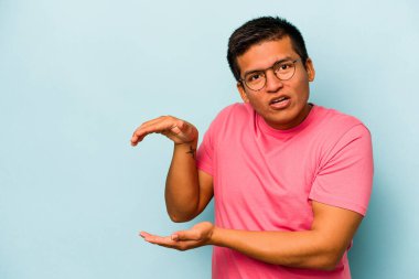 Mavi arka planda izole edilmiş genç İspanyol adam elleri arasında bir kopya alanı tutarken şok oldu ve hayrete düştü..