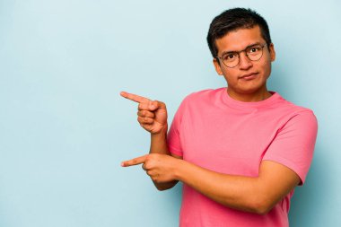 Mavi arka planda izole edilmiş genç İspanyol adam işaret parmağıyla fotokopi alanını işaret ederek şok oldu..