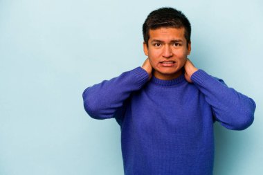 Genç İspanyol bir adam mavi arka planda izole edilmiş kafasının arkasına dokunuyor, düşünüyor ve bir seçim yapıyor..