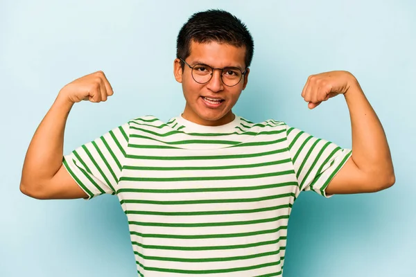 Mavi arka planda izole edilmiş genç bir İspanyol kadın gücünün sembolü olan kollarıyla güçlü bir hareket gösteriyor.