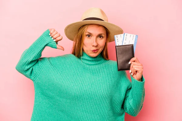 Pembe arka planda izole edilmiş pasaport taşıyan genç beyaz kadın gururlu ve kendinden emin hissediyor, örnek olarak.