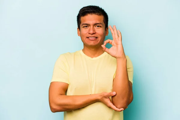 Young Hispanic Man Isolated Blue Background Winks Eye Holds Okay — стоковое фото