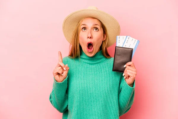 Pembe arka planda izole edilmiş pasaport taşıyan beyaz bir kadın ağzı açık bir şekilde üst tarafı işaret ediyor..