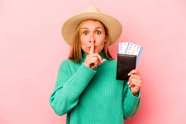 Pasaportu olan beyaz bir kadın pembe arka planda izole edilmiş bir şekilde bir sır saklıyor ya da sessizlik istiyor..