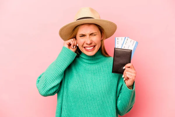 Pasaportu olan beyaz bir kadın pembe arka planda izole edilmiş kulakları elleriyle kapatıyor..