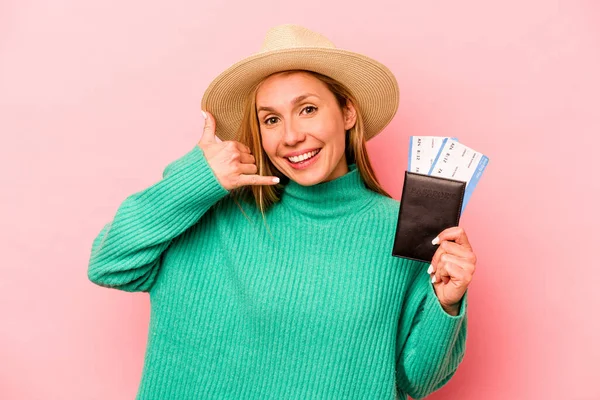 Pembe arka planda izole edilmiş pasaport taşıyan beyaz bir kadın parmakları olan bir cep telefonu hareketi gösteriyor..