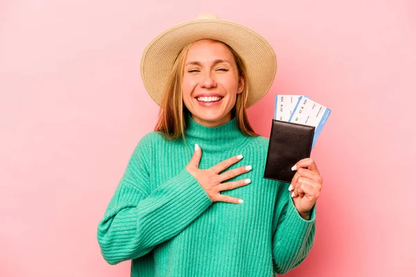 Pembe arka planda izole edilmiş pasaport taşıyan beyaz bir kadın elini göğsünde tutarak kahkahalar atıyor..
