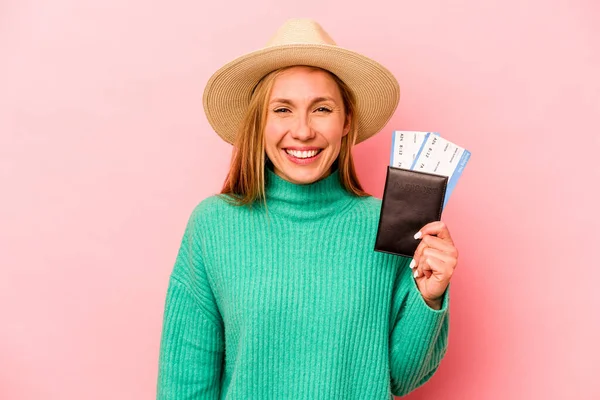 Pasaportu olan beyaz bir kadın pembe arka planda izole edilmiş gülüyor ve eğleniyor..