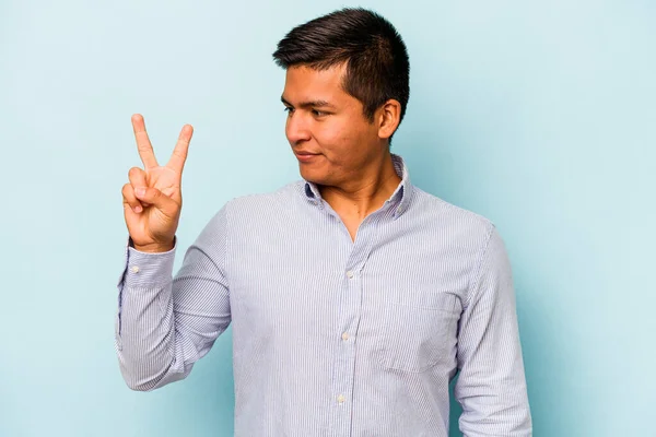 青の背景に孤立した若いヒスパニック系の男喜びと屈託のない指で平和のシンボルを示す — ストック写真