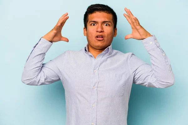 Latin kökenli genç bir adam mavi arka planda zaferi ya da başarıyı kutlarken şaşırmış ve şok olmuştu..