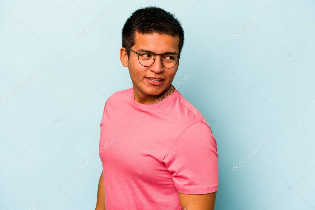 Young hispanic man isolated on blue background looks aside smiling, cheerful and pleasant.