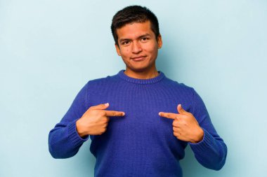 Mavi arka planda izole edilmiş genç bir İspanyol gömlek fotokopisini elle işaret ediyor, gururlu ve kendinden emin.