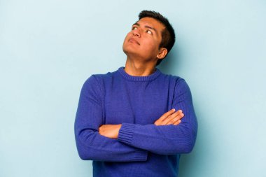 Genç İspanyol adam mavi arka planda izole edilmiş. Amaçlarına ve amaçlarına ulaşmayı hayal ediyor.