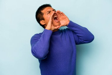 Genç İspanyol adam mavi arka planda izole edilmiş, heyecanlı bir şekilde bağırıyor..