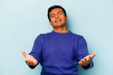 Mavi arka planda izole edilmiş genç bir İspanyol hoş geldin ifadesi sergiliyor..