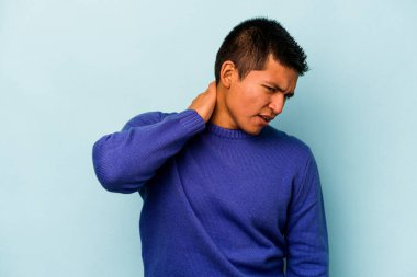 Genç İspanyol bir adam mavi arka planda izole edilmiş, sabit yaşam tarzından dolayı boyun ağrısı çekiyor..
