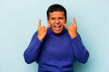 Genç İspanyol asıllı bir adam mavi arka planda izole edilmiş boynuzları bir devrim konsepti olarak gösteriyor..