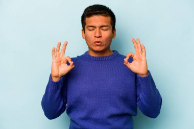 Mavi arka planda izole olmuş genç İspanyol adam sıkı çalışma gününden sonra rahatlıyor, yoga yapıyor..